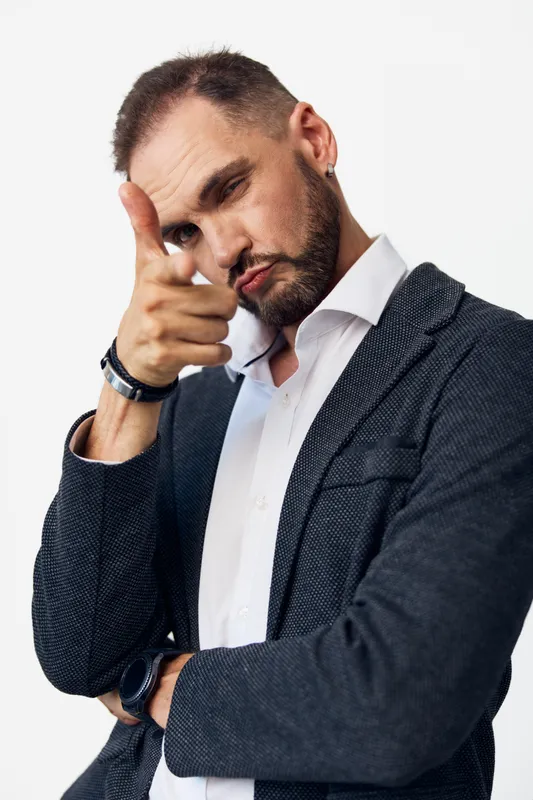 A confident business professional man poses with a playful finger gun gesture against an isolated light colored background, conveying focus, motivation, and assertive attitude.