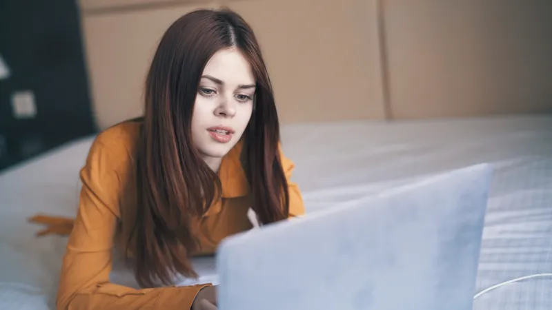 Женщина в спальне лежит на кровати перед ноутбуком, работая в интернете