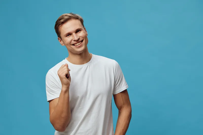 smiling happy young caucasian man hold smartphone look camera wearing white t-shirt isolated blue background digital nomad concept