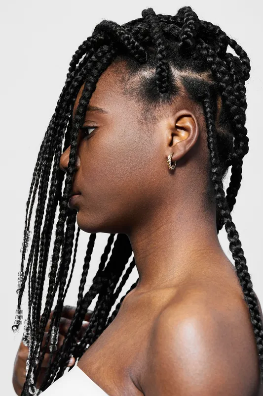 Profile portrait of a Black woman with long braids showcasing beauty and confidence against a light background, highlighting modern hairstyle trends and self expression