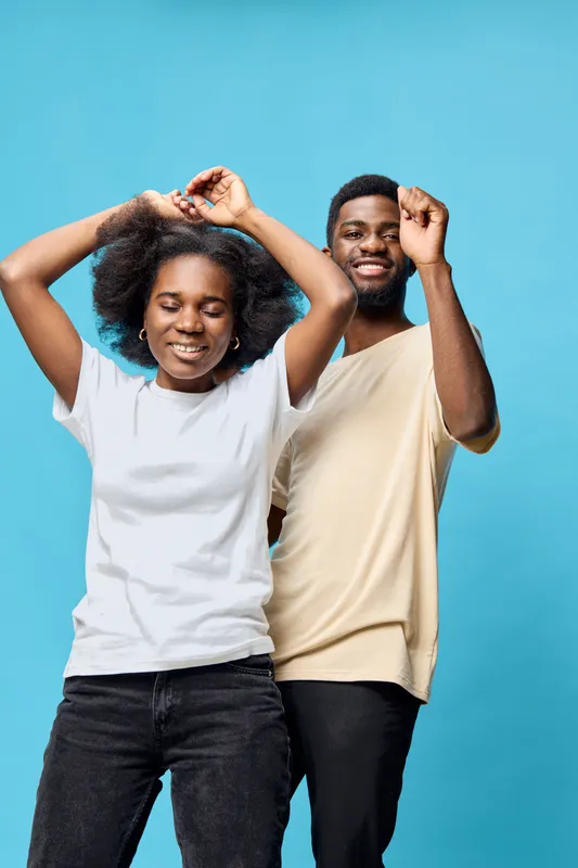 Joyful young African American couple dancing against a bright blue background, wearing casual clothing, showcasing happiness and connection during a fun moment