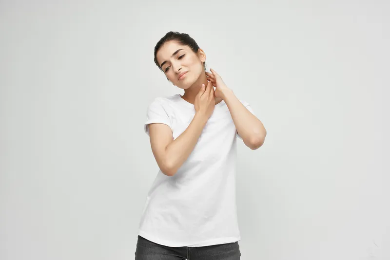 Женщина держится за шею, испытывая боль, и принимает лекарства от мигрени