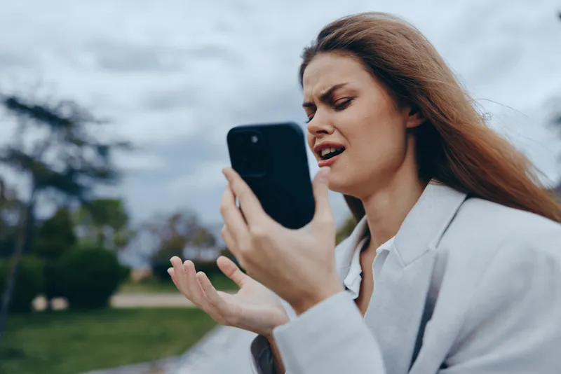 upset woman holding smartphone with frustrated expression outdoors during cloudy weather upset woman smartphone frustration emotion outdoor autumn season business concept