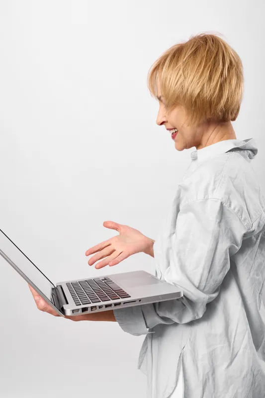 Blonde child with open computer laptop on white background, side view, hands gesture near keyboard, focused on screen for technology learning and education at home