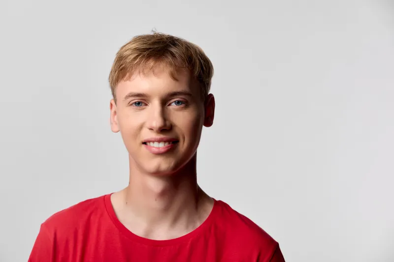 Young man in a red shirt smiles against a neutral background, emitting friendliness, confidence and approachable professionalism for lifestyle and headshot use