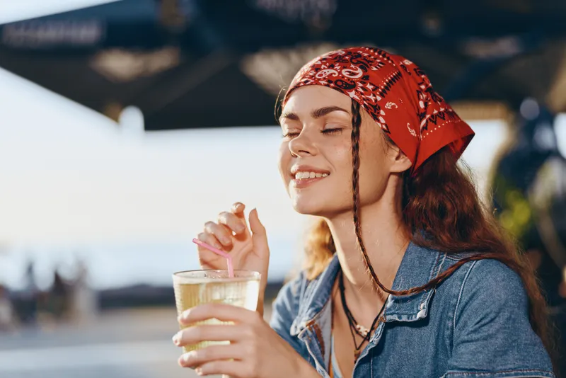 lifestyle woman enjoying refreshing drink in modern boho-western denim street style with film color tones, relaxed outdoors, summer vibes