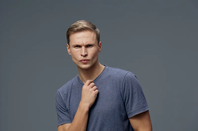 Portrait serious man in casual t-shirt thinking looking camera indoor studio gray background mental health gadgets concept