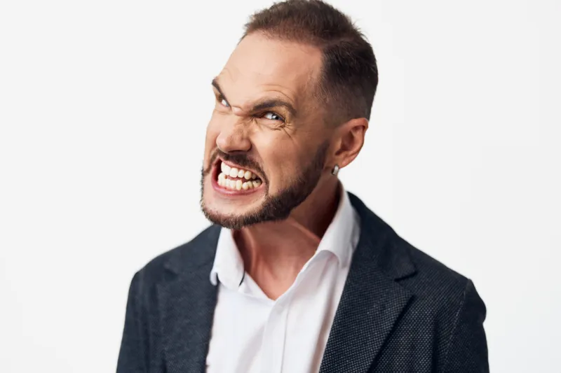 A focused business professional man with a bold, tense expression stands against an isolated colored background, showing intense emotion. This portrait conveys drive, leadership, and resilience for