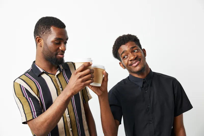 Two black men enjoying coffee together, showcasing friendship and joy. Bright colors and casual attire create a vibrant and relaxed atmosphere.