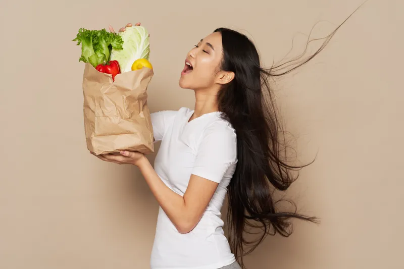 В руках женщины находится пакет с продуктами, здоровой пищей, овощами, что символизирует диету, на бежевом фоне