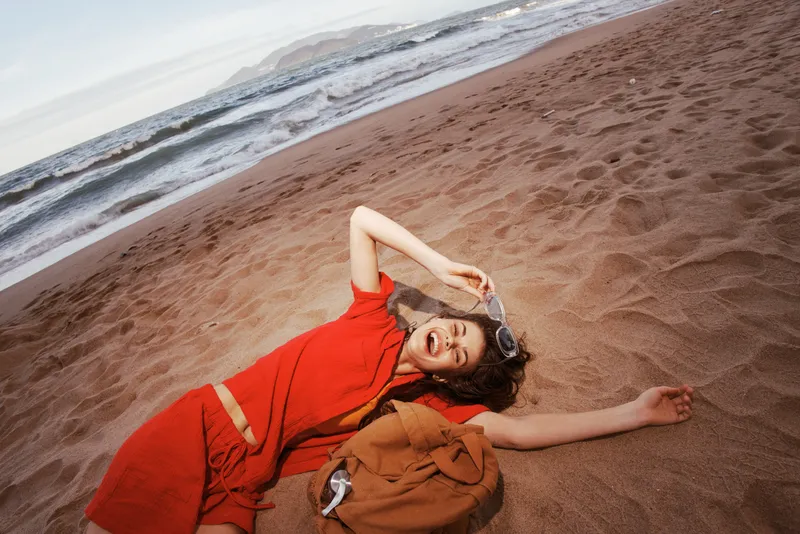 Радостная путешественница: беззаботная девушка с рюкзаком гуляет по солнечному пляжу, наслаждаясь опьяняющей красотой природы