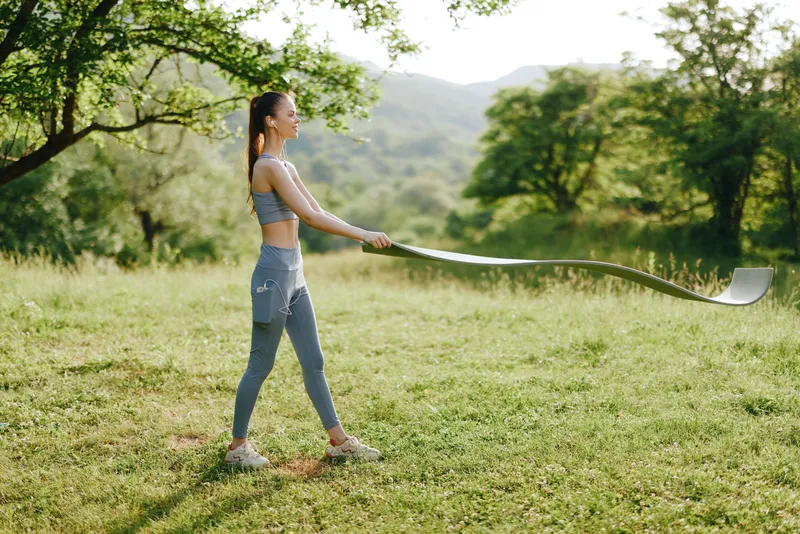 Young athletic woman exercising with a long resistance band outdoors in a green meadow, showcasing strength and determination during a sunny day