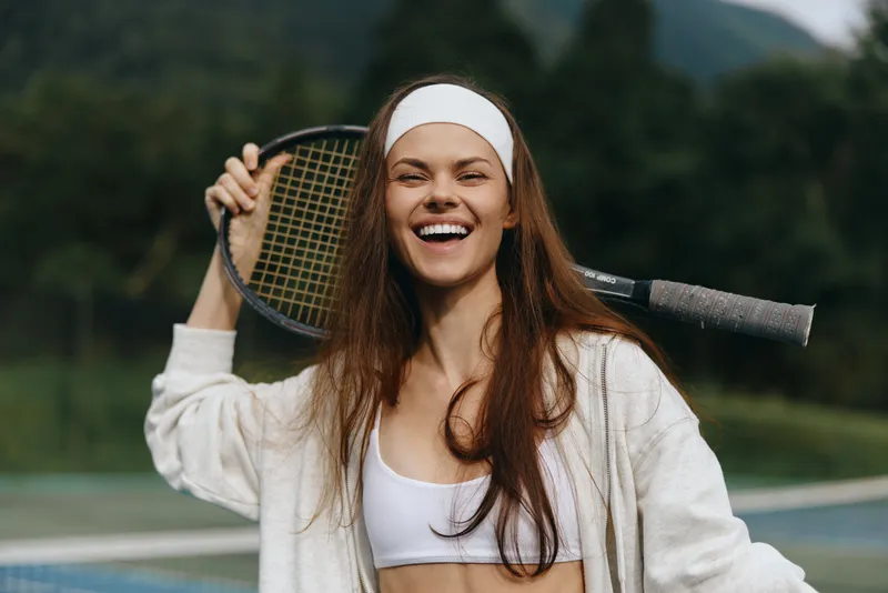 Happy female tennis player celebrating victory outdoors with a racket in hand, wearing sporty clothing, surrounded by nature in a vibrant green background