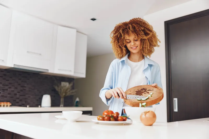Женщина с вьющимися волосами стоит перед столом с тарелкой еды у себя дома