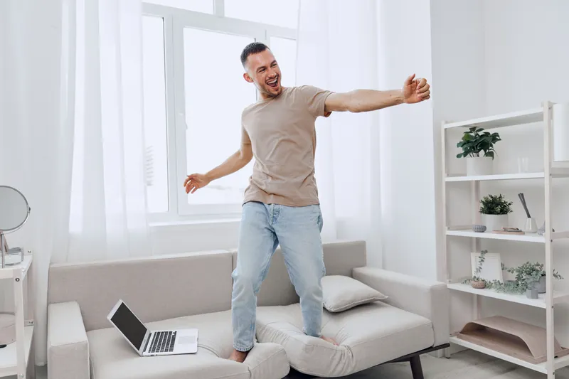 Joyful man dancing at home, embracing digital detox and work-life balance, enjoying life’s authentic moments in a relaxed environment.