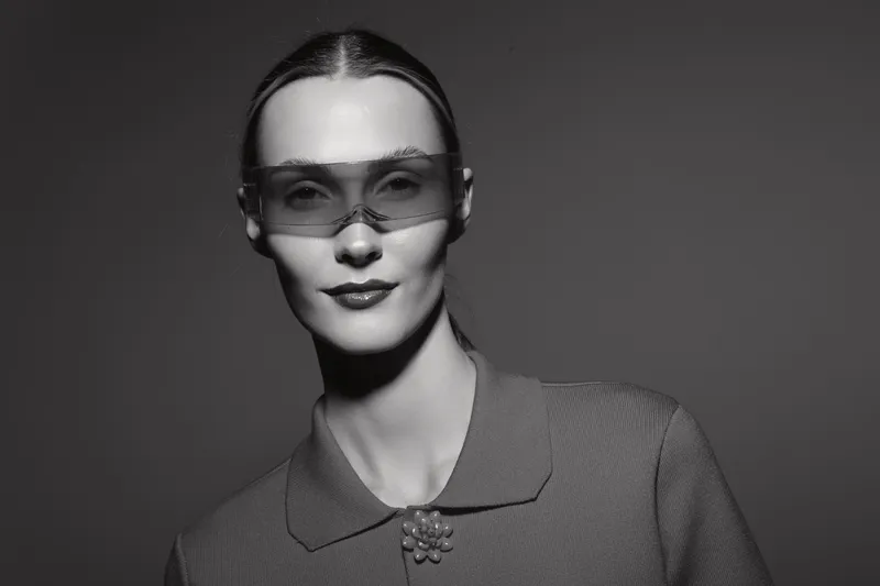 Portrait of a white woman with fair skin wearing stylish glasses and textured clothing in a studio with moody lighting.