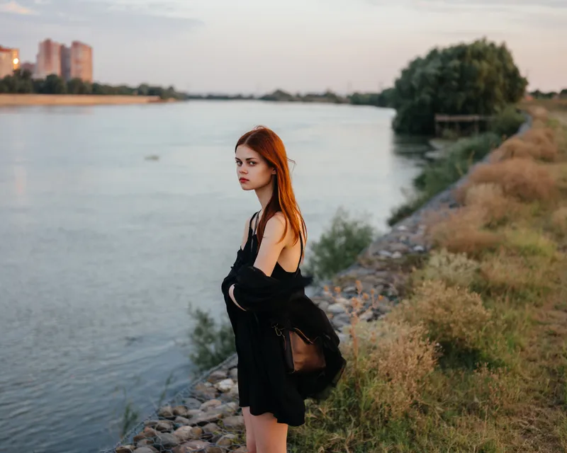 Рыжеволосая женщина в черном платье идет по природе, демонстрируя модный образ