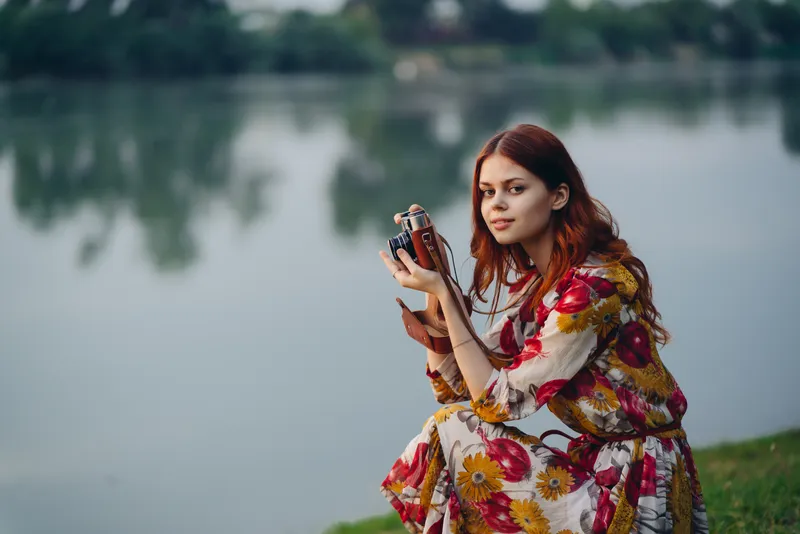 Женщина с фотоаппаратом на природе у реки во время отпуска или путешествия