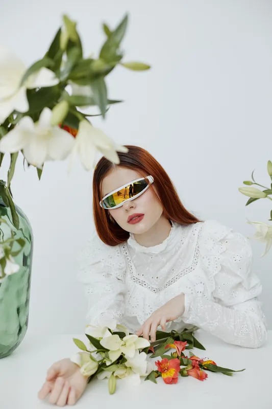 Elegant woman wearing stylish sunglasses with flowers on a white background, showcasing a modern and fresh aesthetic