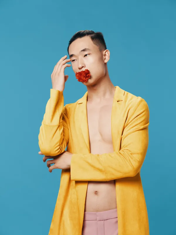 Мужчина с красным цветком во рту, в жёлтой куртке, с обнажённым торсом на синем фоне