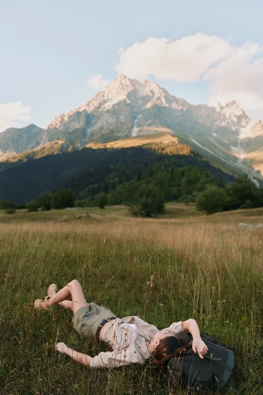 Woman relaxing in a meadow with distant mountains, showcasing outdoor lifestyle, nature appreciation, and carefree leisure.