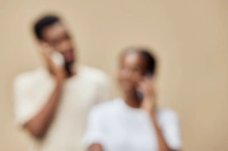 Young African couple communicating on smartphones, expressing emotions with a soft, neutral background that highlights their interaction and connection