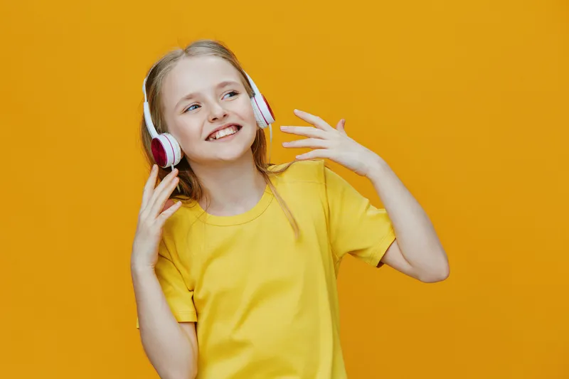 Happy girl enjoying music with headphones on a bright yellow background, wearing a cheerful yellow t shirt, embodying youthful joy and positivity