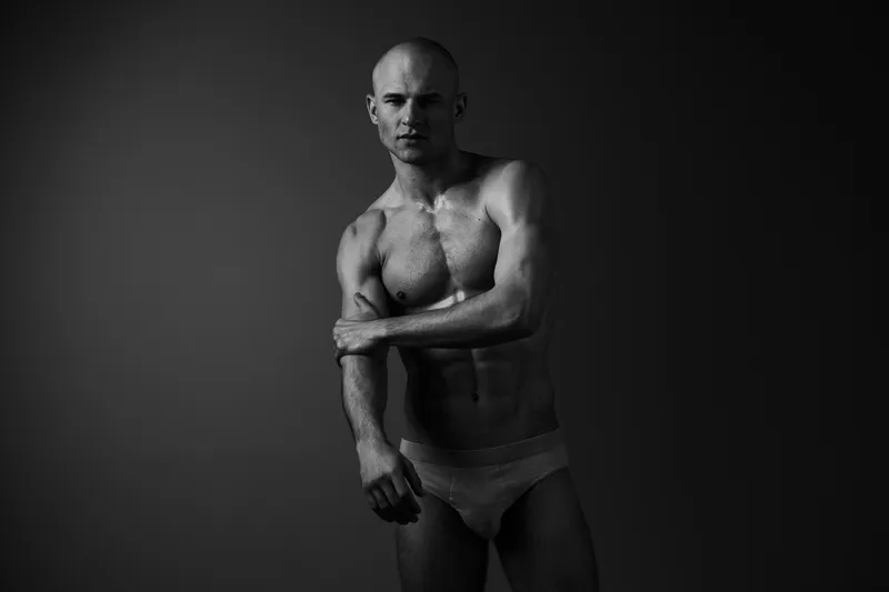 Black and white portrait of a confident man, showcasing strong physique and striking pose, emphasizing emotions of strength and determination.