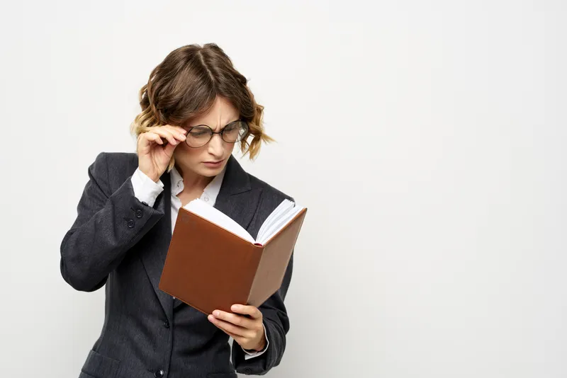Женщина на работе с книгой в руке, светлый фон, классический костюм, очки, голова