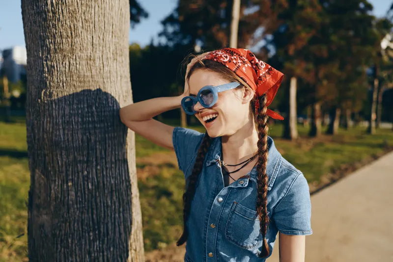 Lifestyle woman in modern boho-western denim street style smiling outdoors with film color effect and casual accessories under natural sunlight.