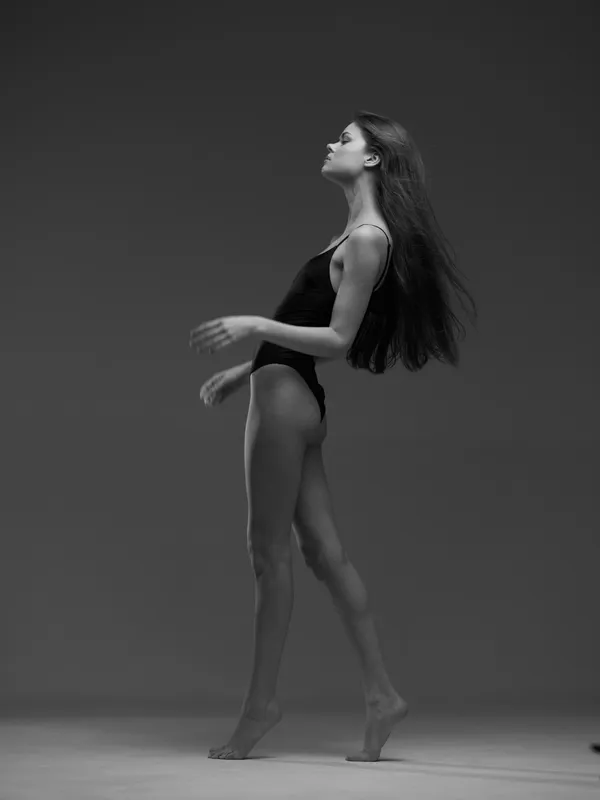 Black and white elegant woman in bodysuit posing against gray background in studio lighting.