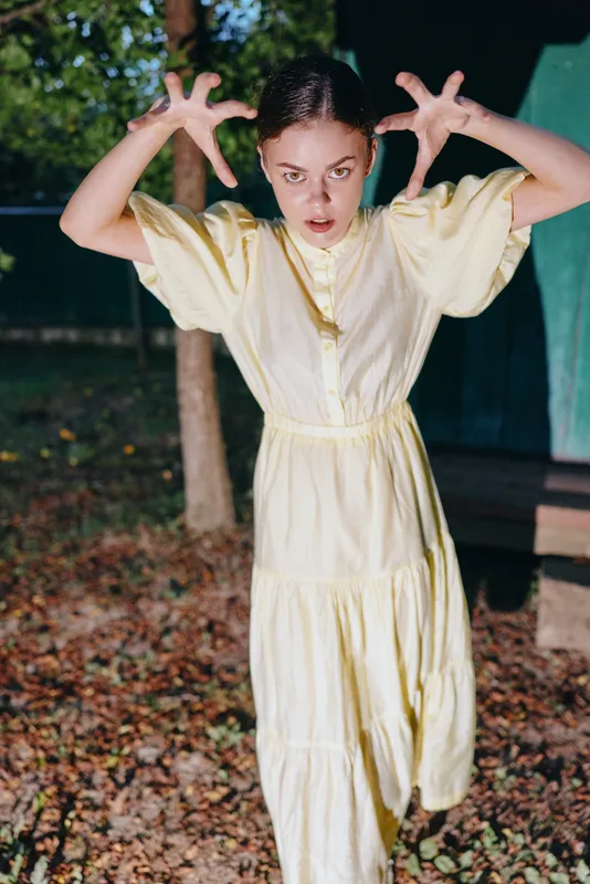 Girl child in yellow dress makes scary pose with intense expression outdoors at night, playful acting with authenticity inclusivity and natural emotion and gentle play