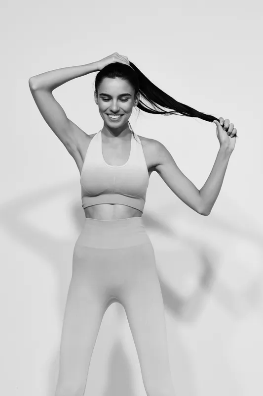 Sport fitness woman tying her hair in black and white photo, wearing seamless activewear, relaxed and focused with minimalistic studio background.