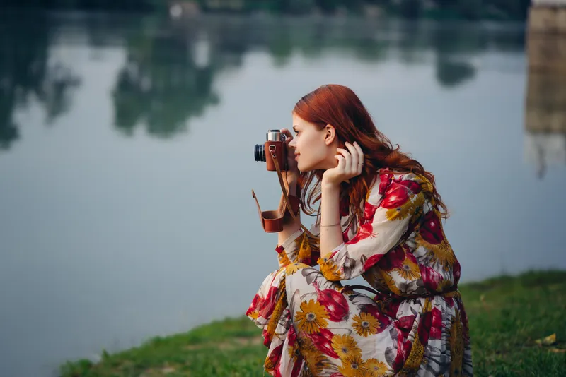 Женщина в платье с фотоаппаратом на природе, фотографирует реку, хобби