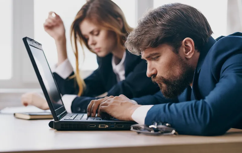 Уставшие мужчина и женщина, коллеги по работе, работают за ноутбуком