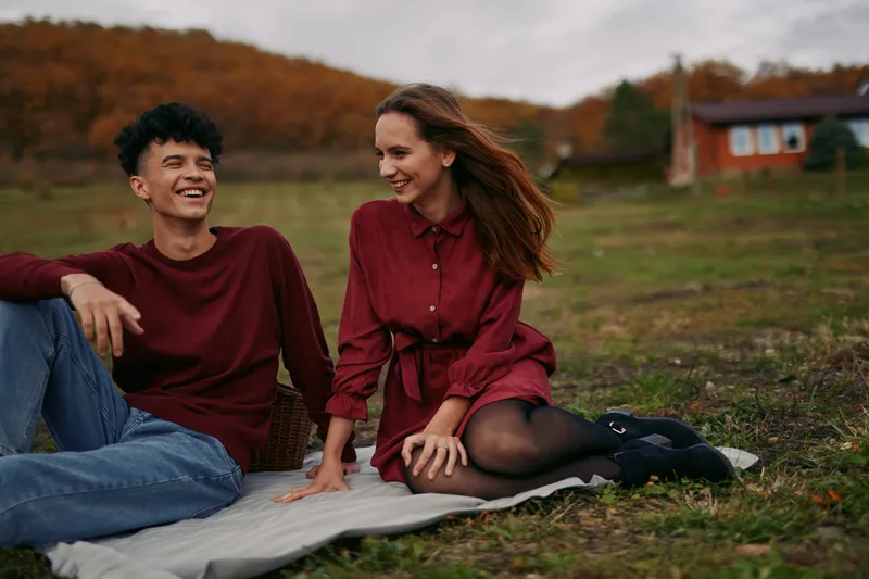An authentic moment with two friends sharing a blanket in an autumn field, capturing authenticity and genuine emotion through candid smiles, warm light, and natural connection.