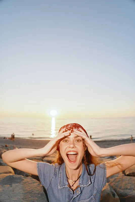 excited woman on beach at sunset with joyful expression and casual outfit enjoying warm evening light by the calm sea shore