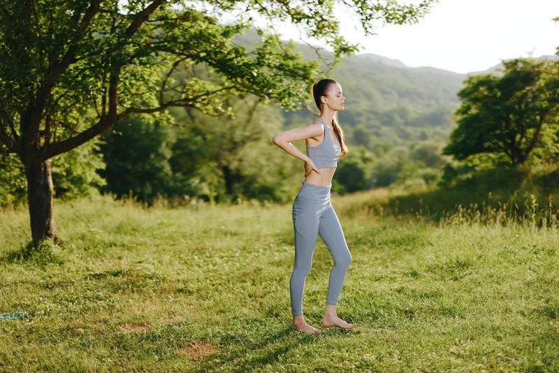 Athletic woman stretching outdoors in a serene green landscape, wearing a fitted sports bra and leggings, embodying health and fitness