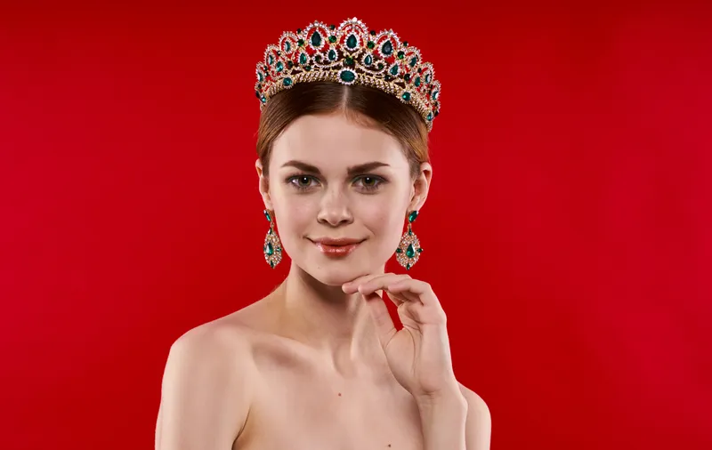Портрет уверенной женщины на красном фоне с короной на голове