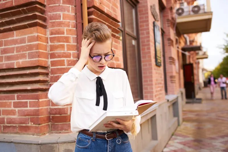 Коротко стриженная женщина с книгой в руках читает на открытом воздухе