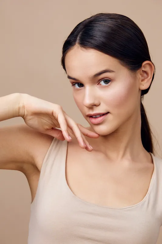 Beautiful young woman with natural makeup poses gracefully, showcasing healthy skin tone against a soft neutral background Captures beauty and serenity