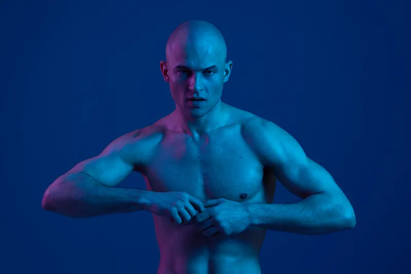 Athletic man with a confident pose, showcasing toned muscles under dramatic lighting. The vibrant colors highlight strength and determination in this striking image.