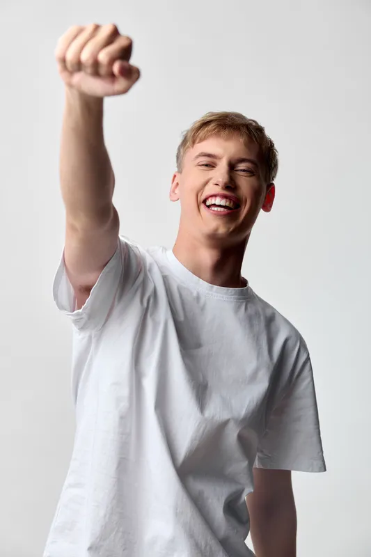 Victory, celebration, and confidence as a cheerful man raises his fist in a casual white t-shirt, capturing energy, mood, and triumph in a dynamic studio shot