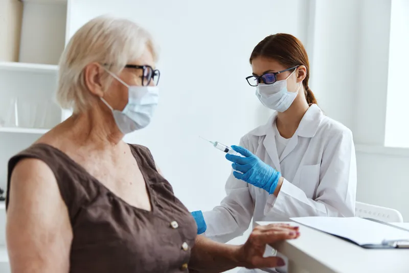 Женщина-врач делает укол в плечо для вакцинации и проверяет паспорт вакцинации