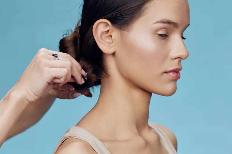 Portrait of a young woman with a stylish updo hairstyle on a light blue background, showcasing professional hairstyling techniques and modern beauty aesthetics