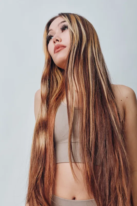 Young woman with long straight hair in beige top posing with soft natural makeup against white background for beauty and fashion concept.