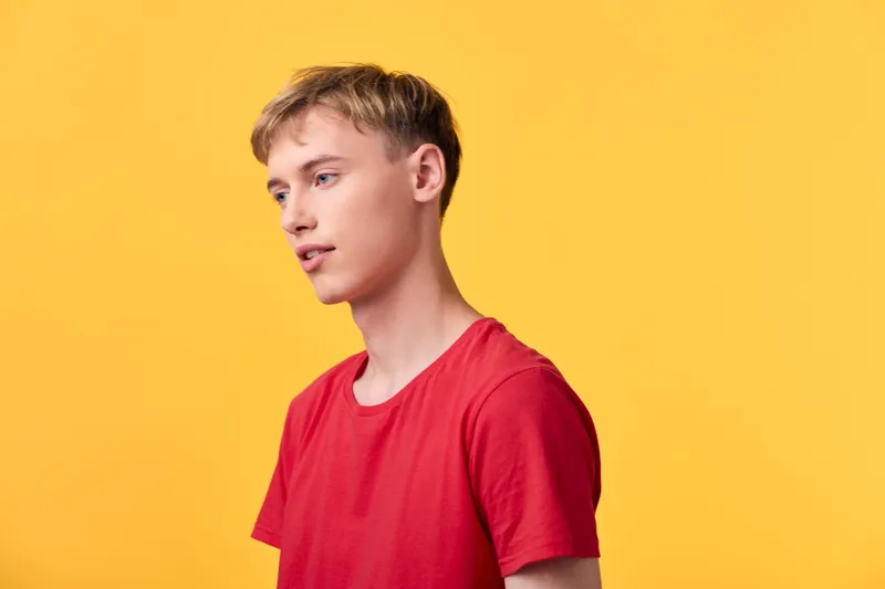 Young man in a red shirt stands in a studio with a yellow background, showcasing casual fashion, modern style, and vibrant color contrast for lifestyle and product imagery