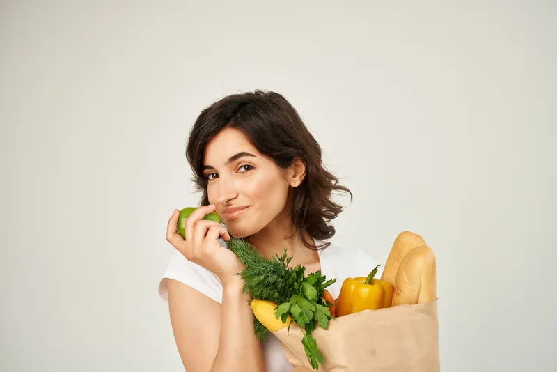Улыбающаяся женщина с пакетом продуктов в супермаркете на светлом фоне