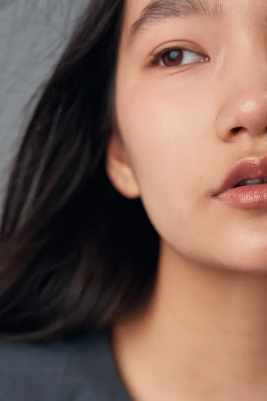 Woman portrait closeup with bare face and natural expression showing smooth skin and dark hair, isolated with soft lighting on neutral background for beauty or skincare concept.