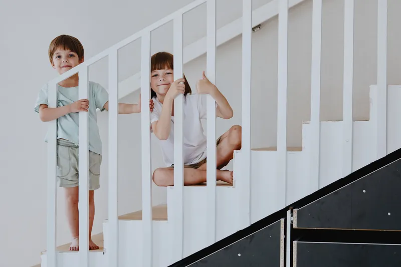 Two cheerful boys playfully posing on a staircase, showcasing their playful spirit and friendship in a bright, inviting interior space.